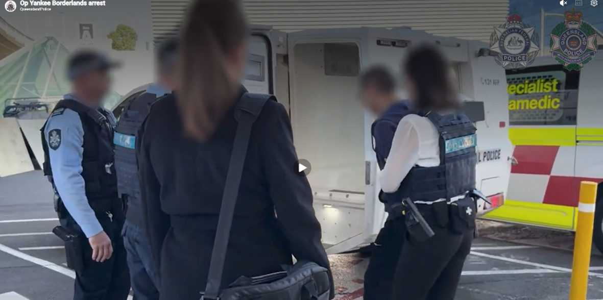 A man is led into a police wagon by five law enforcement personnel. All faces are blurred.
