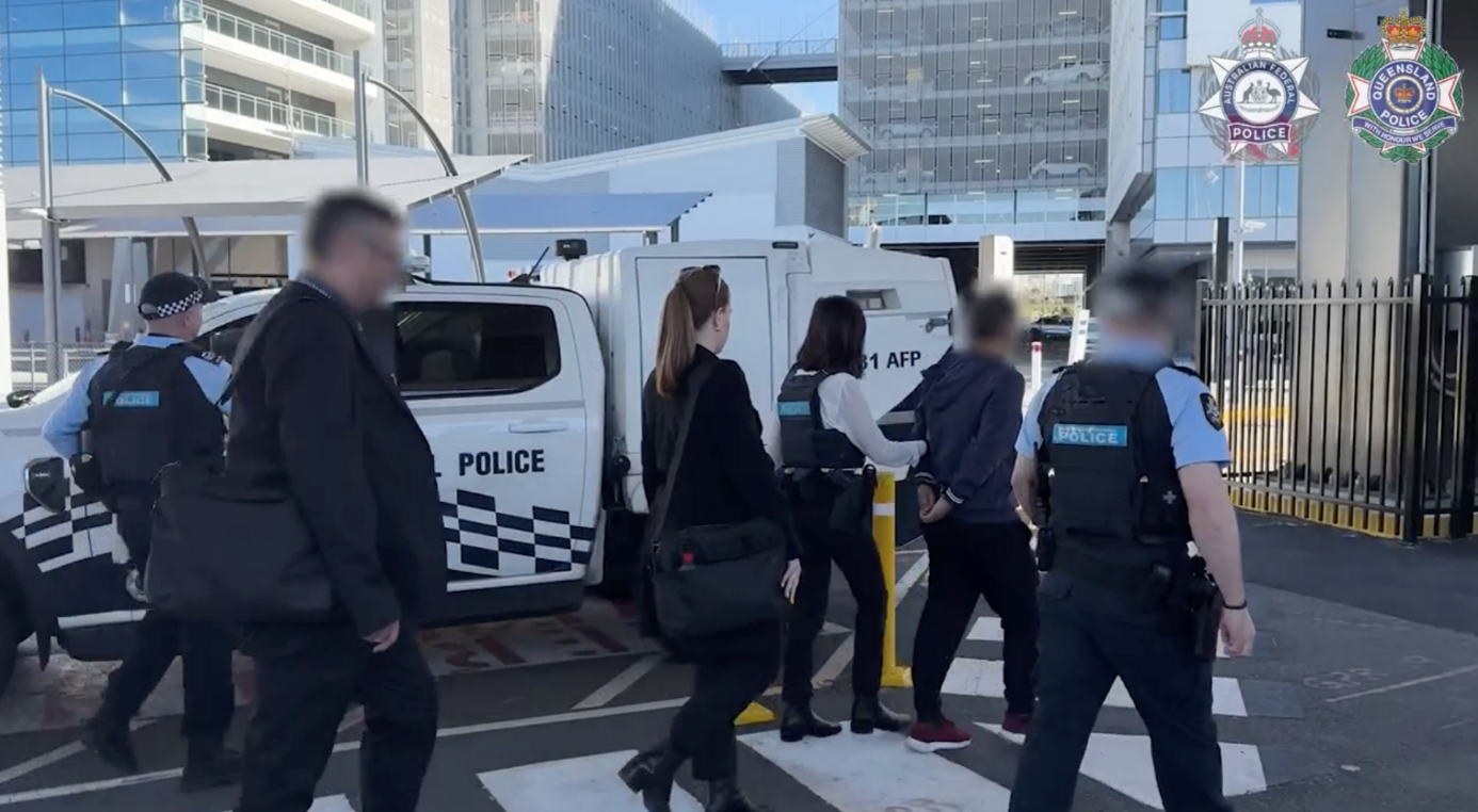A man in handcuffs is led away, flanked by law enforcement officials.